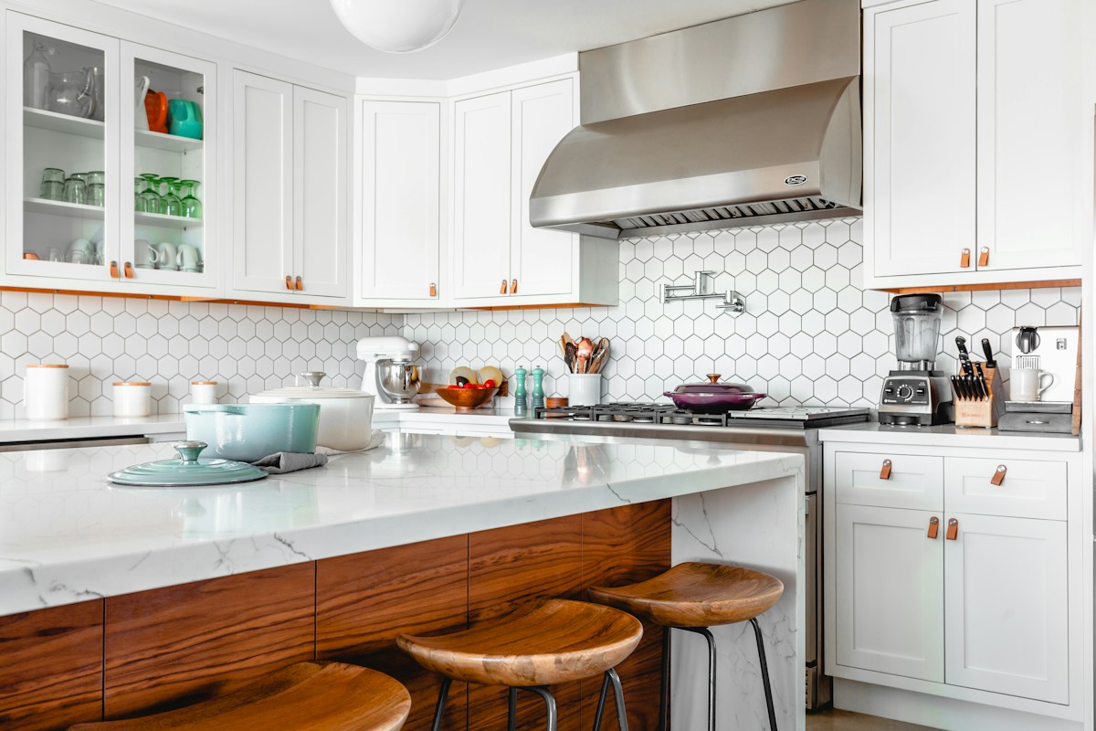 Kitchen with white cabinetry, a marble island, and wood stools; stock photograph